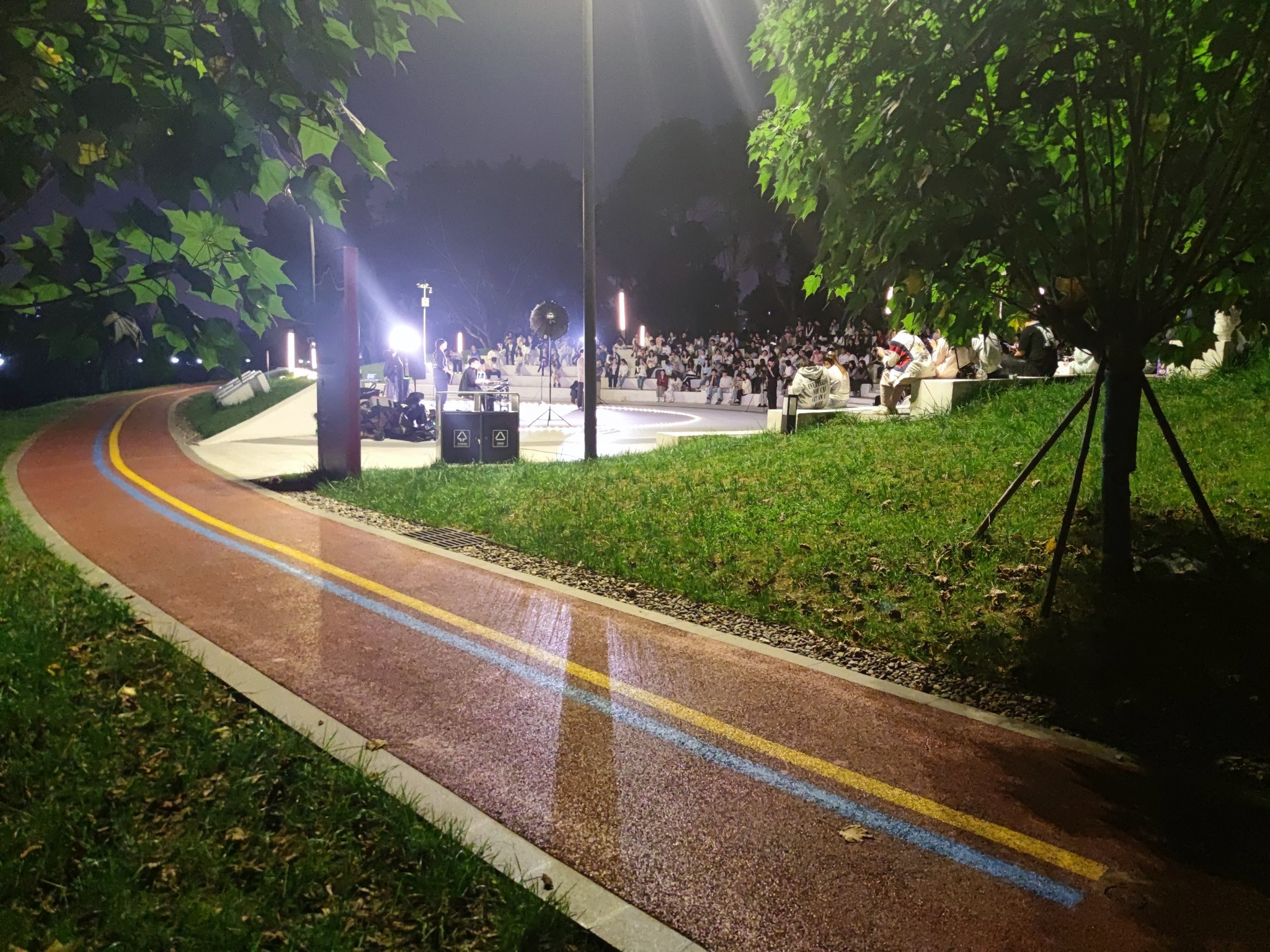 夜色中，树木与步道旁亮着灯的露天活动现场
